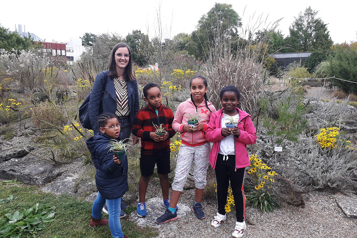 Kinder und Caritasmitarbeiterin stehen im botanischen Garten und halten Pflanzen