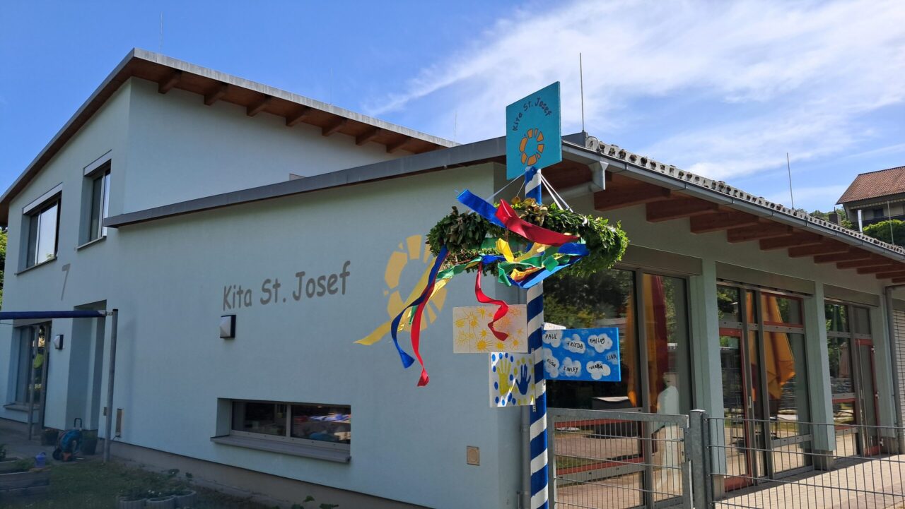 Von Team und Kindern gestalteter Maibaum steht vor dem Gebäude der KiTa St. Josef im Garten der KiTa