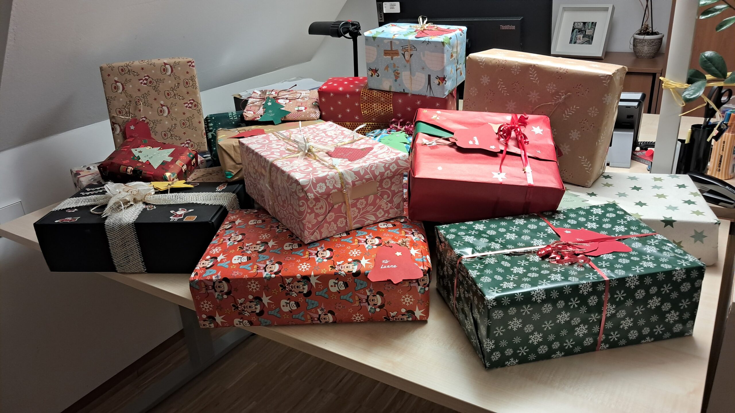 Geschenke liegen gestapelt auf einem Schreibtisch.